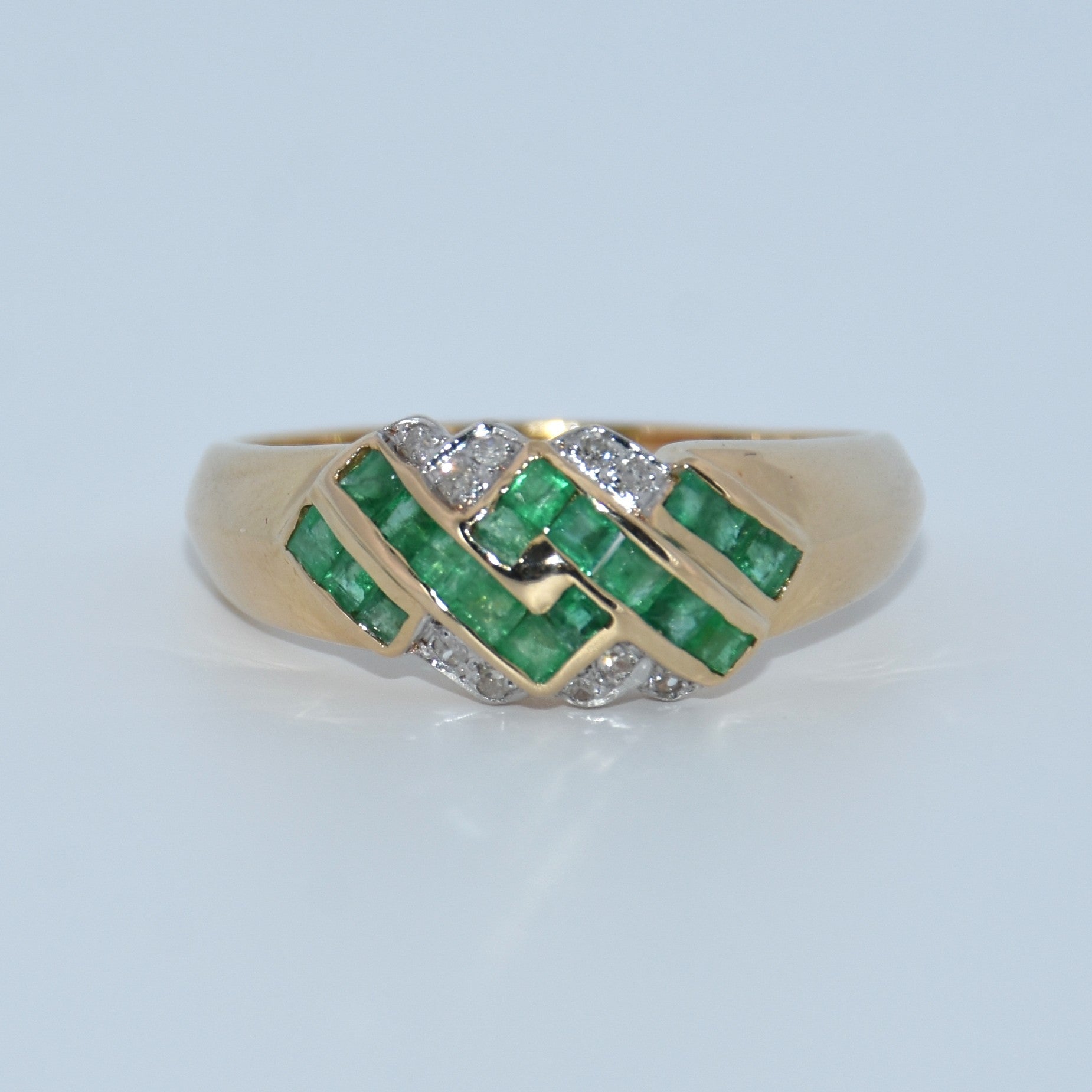 Gold ring with emeralds and diamonds on a light gray background