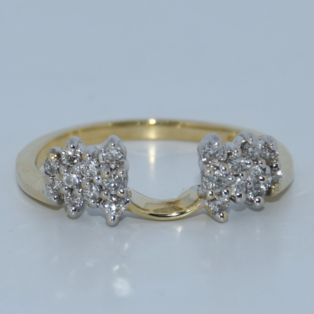Gold ring with diamond clusters on a light gray background