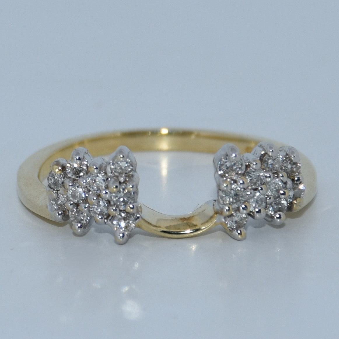 Gold ring with diamond clusters on a light gray background
