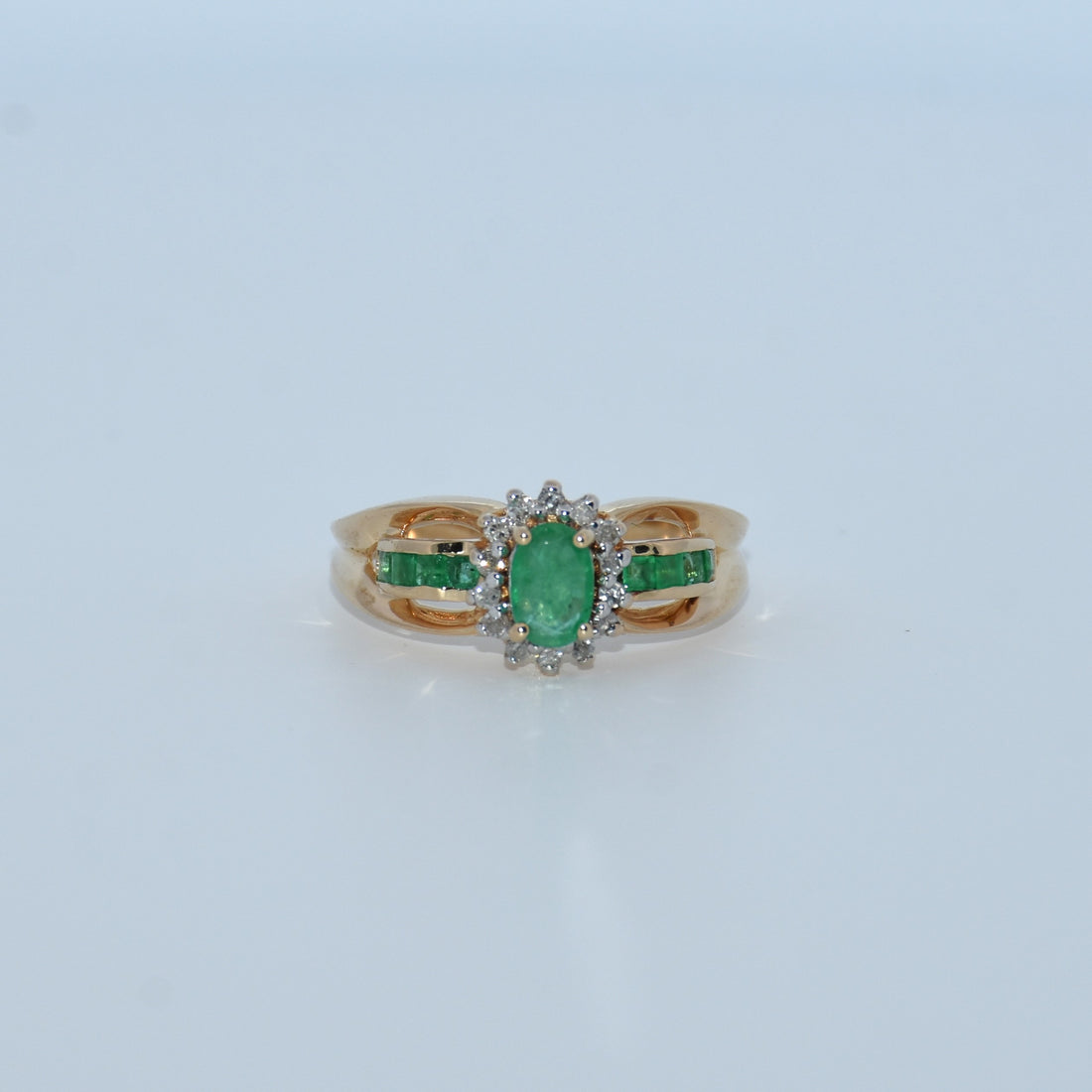 Gold ring with emerald and diamond accents on a light gray background