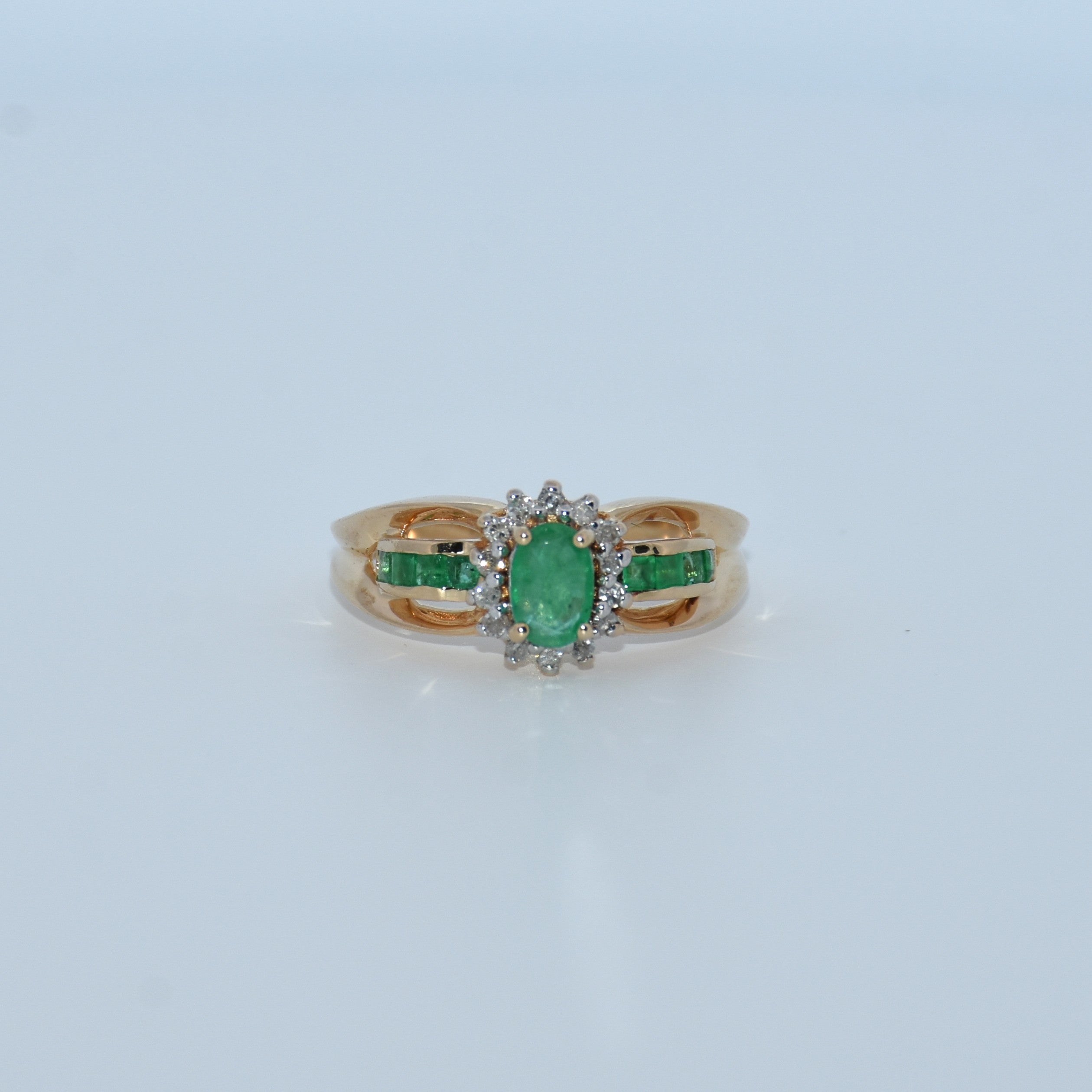 Gold ring with emerald and diamond accents on a light gray background