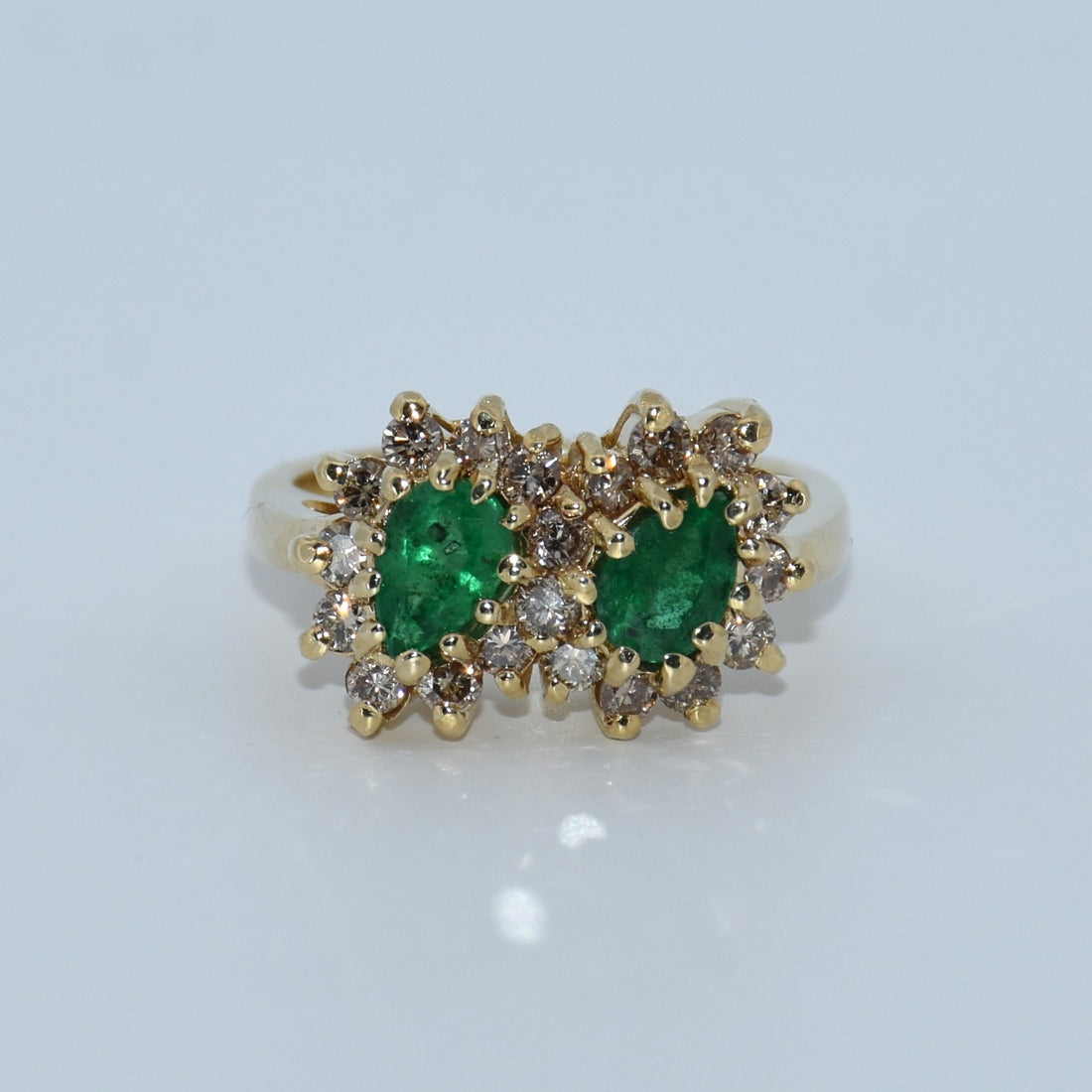 Gold ring with emeralds and diamonds on a light gray background