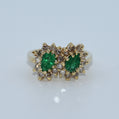 Gold ring with emeralds and diamonds on a light gray background