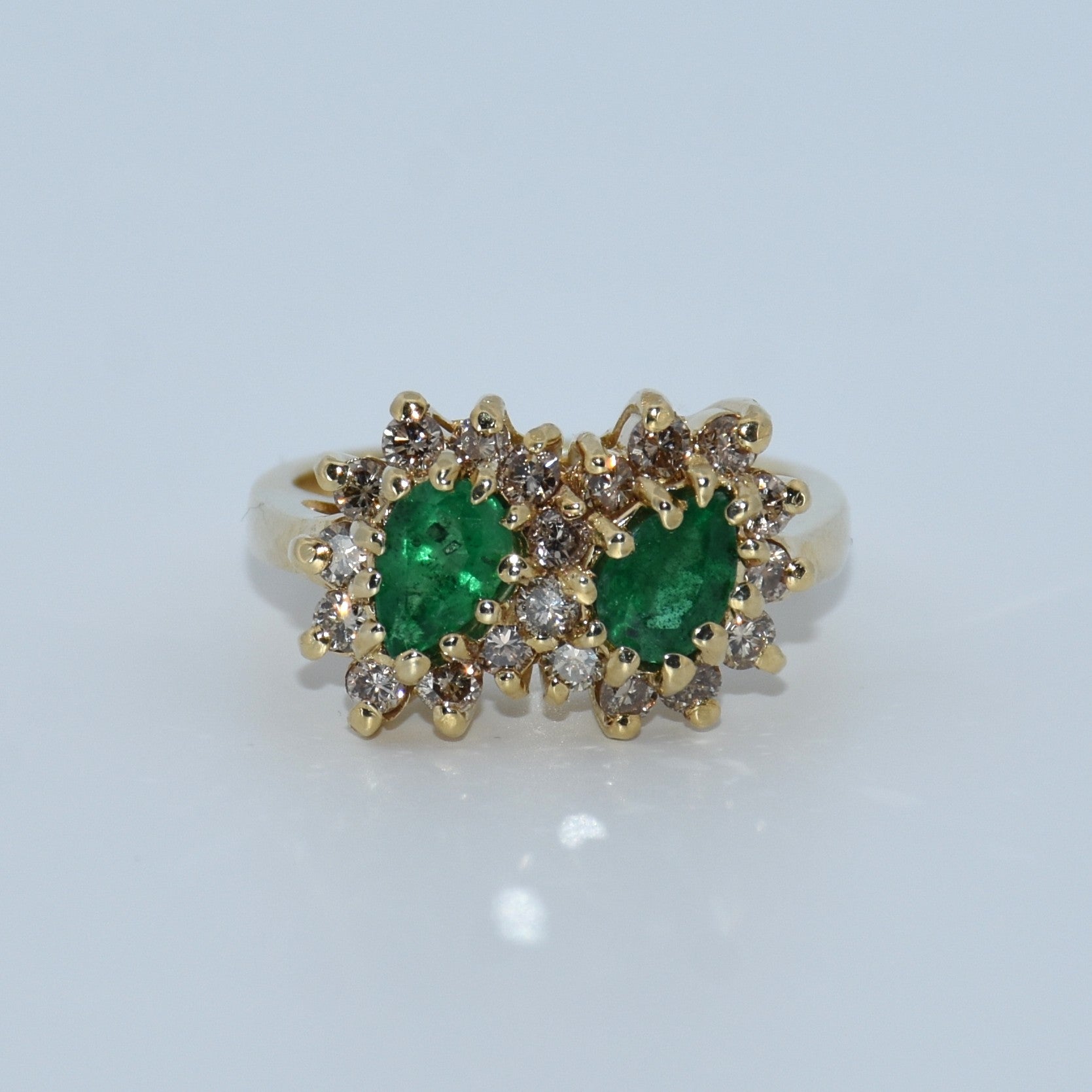 Gold ring with emeralds and diamonds on a light gray background