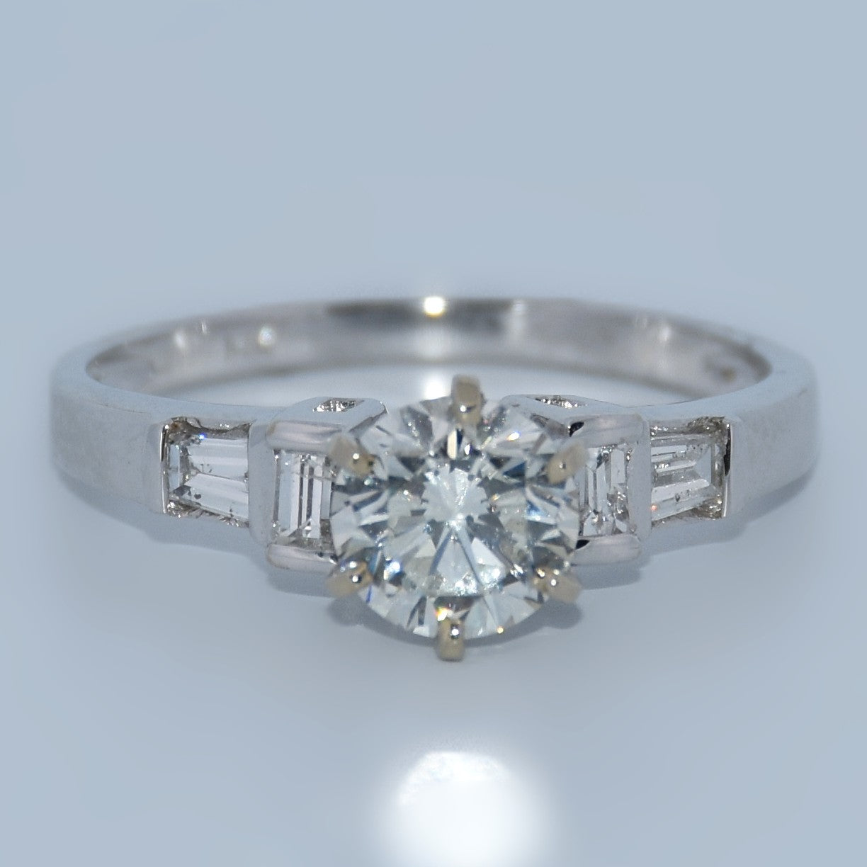 Diamond ring with a central diamond and baguette-cut side stones on a light gray background