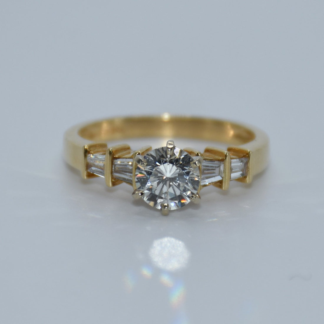Gold ring with a diamond and baguette-cut gemstones on a light gray background