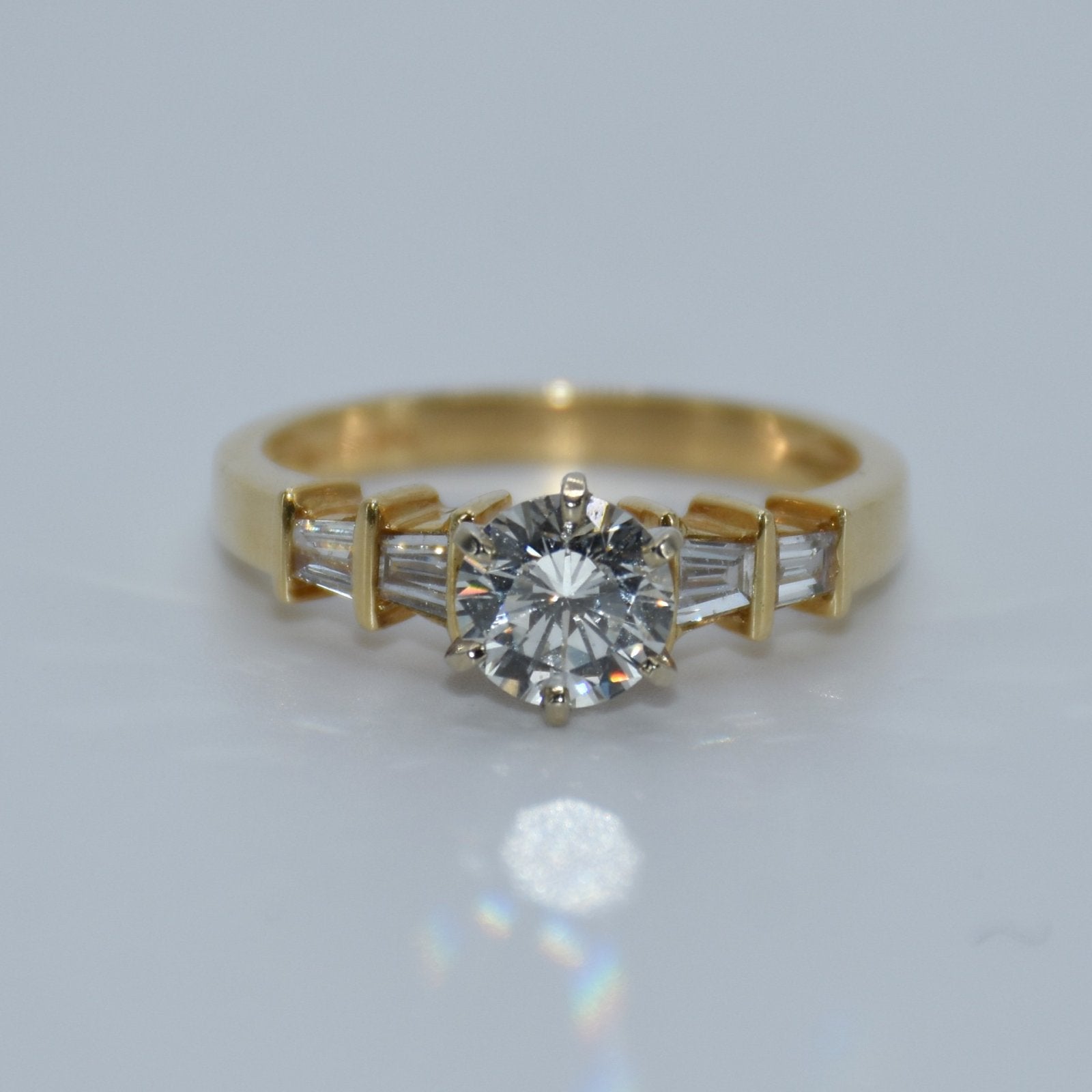 Gold ring with a diamond and baguette-cut gemstones on a light gray background