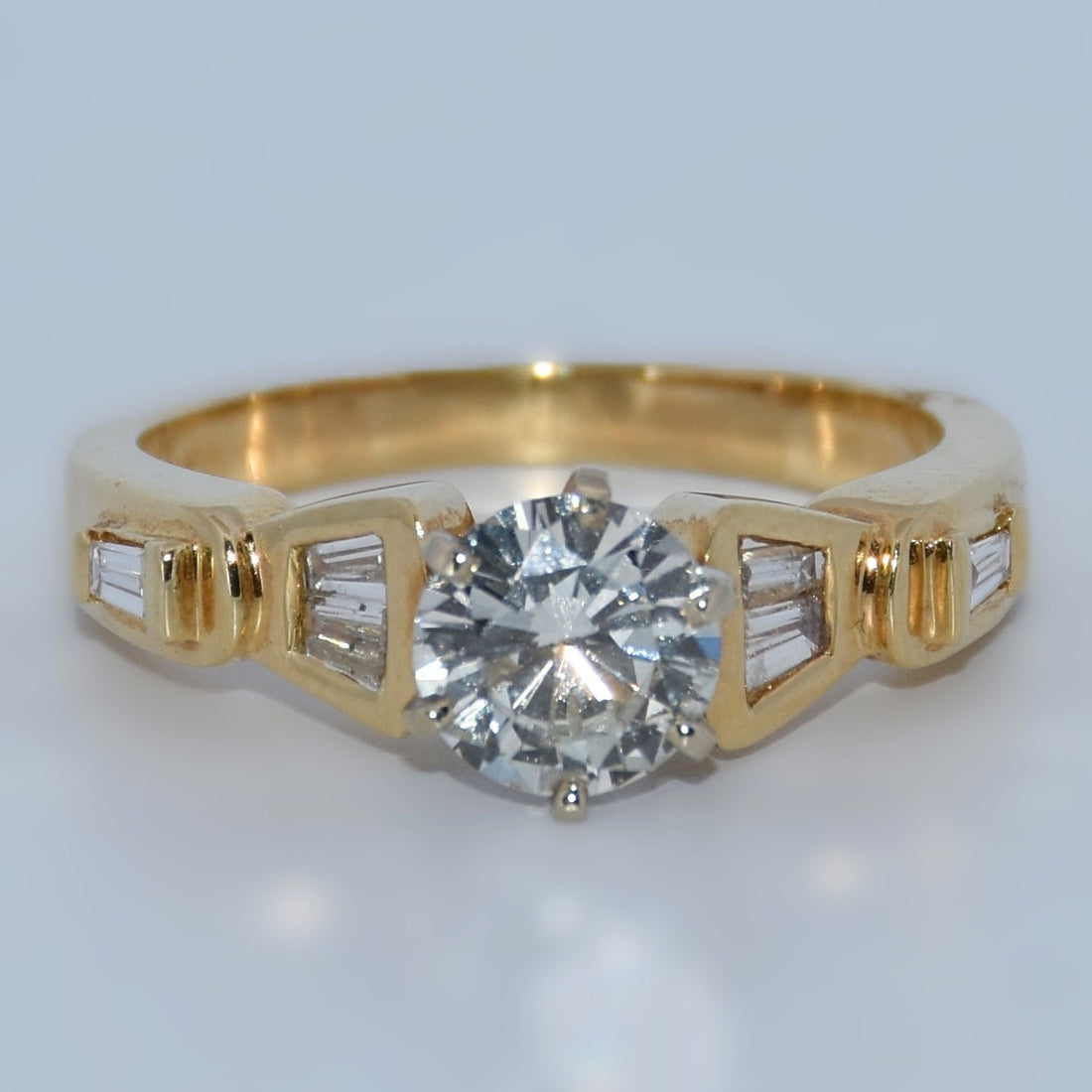 Gold ring with a large diamond and smaller baguette-cut diamonds on a light gray background