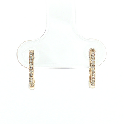 A pair of small gold huggie hoop earrings with a row of clear stones, displayed on a clear plastic jewelry stand against a white background.