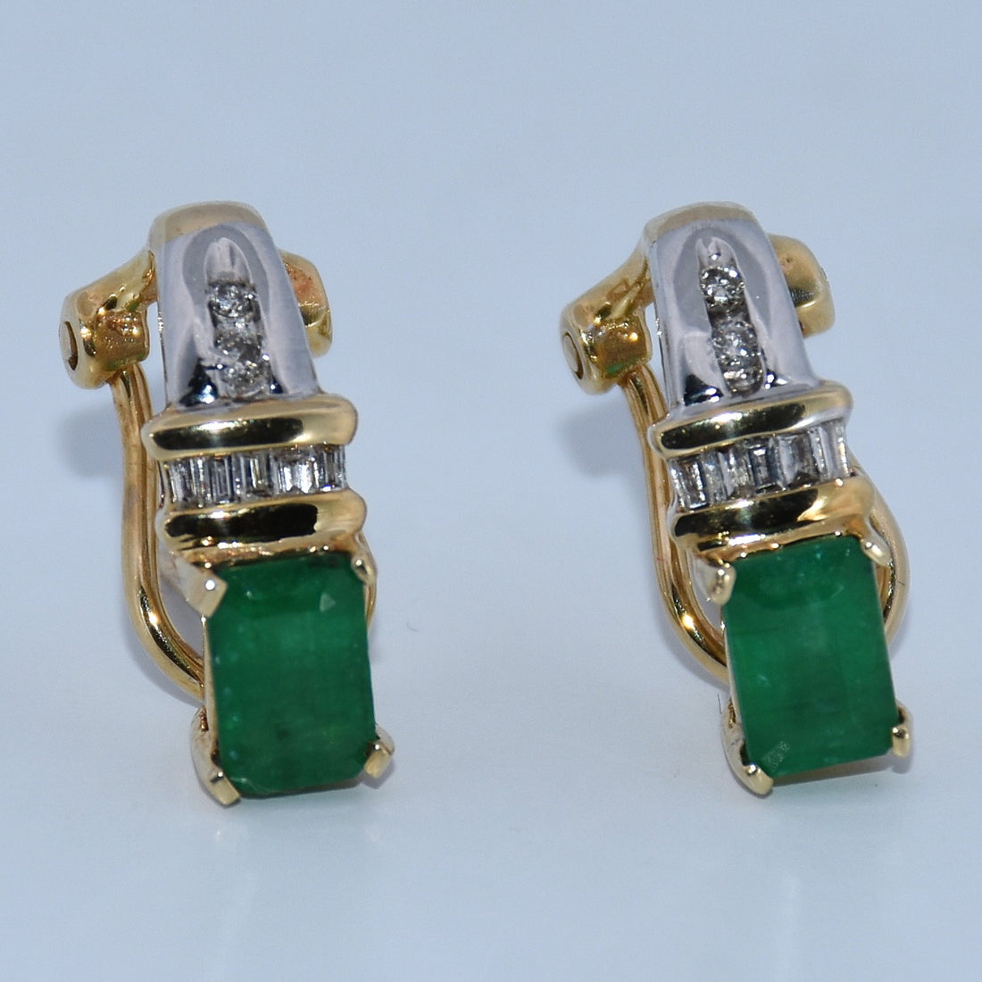 Gold and silver earrings with green gemstones on a light gray background