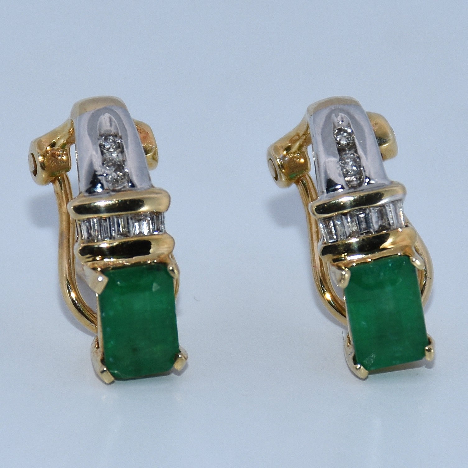Gold and silver earrings with green gemstones on a light gray background