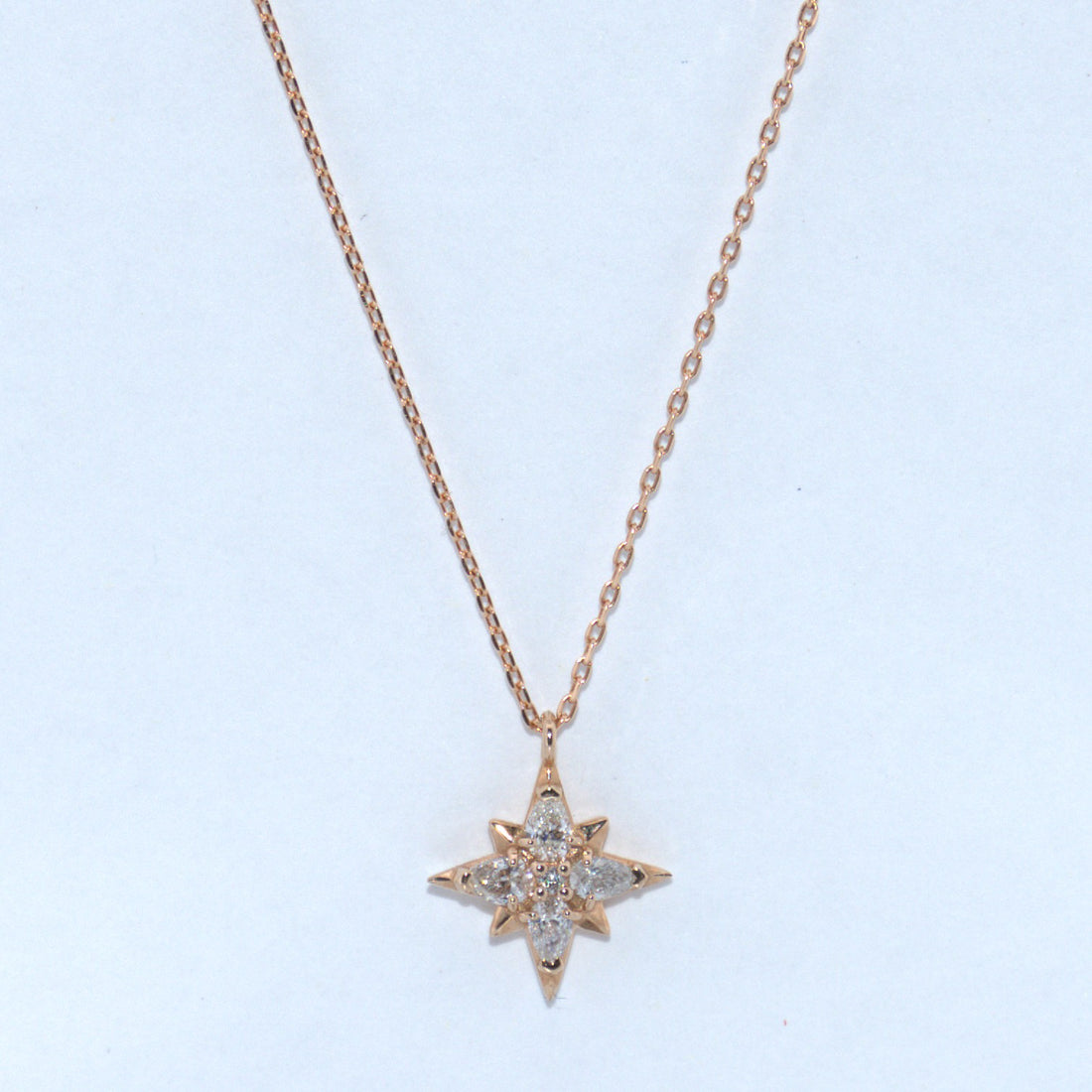 Star-shaped diamond pendant on a rose gold chain against a light blue background
