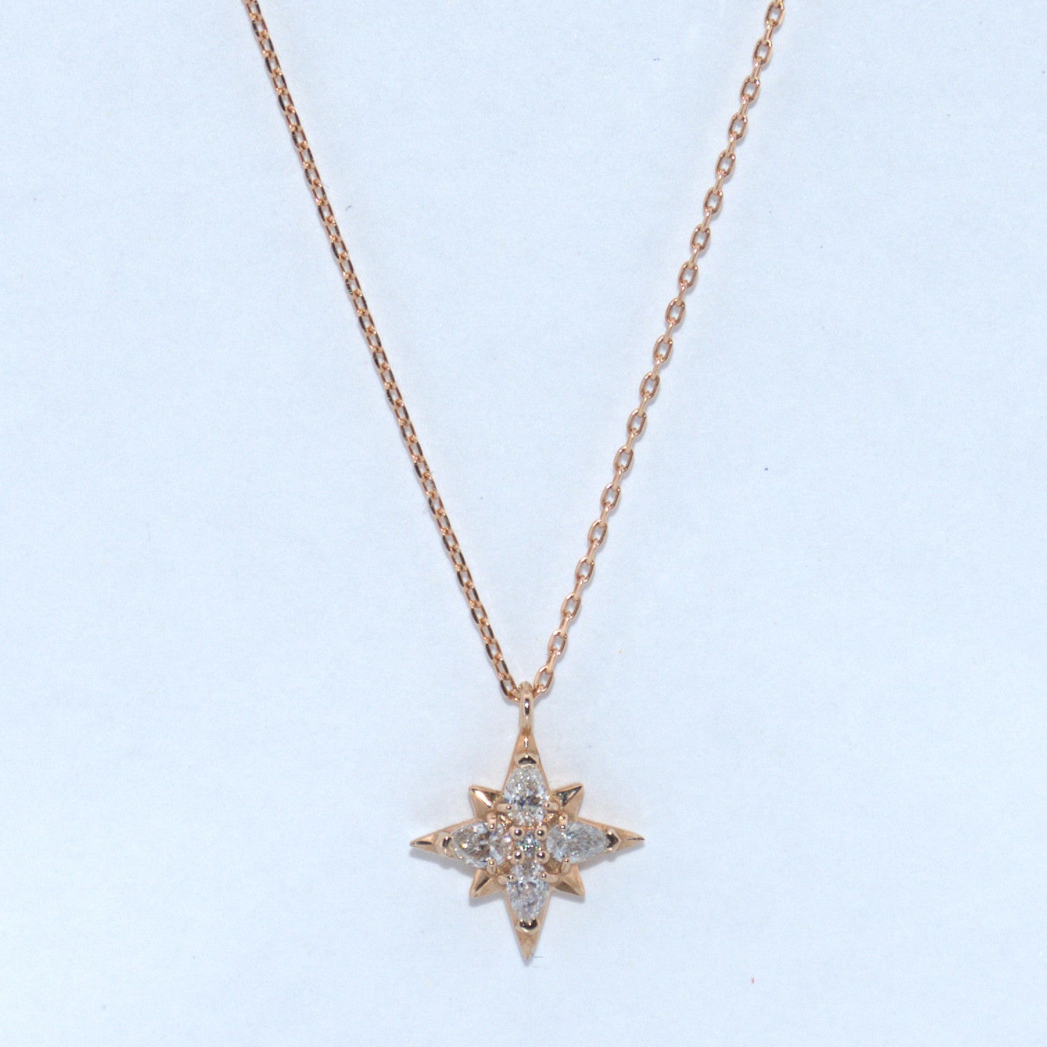 Star-shaped diamond pendant on a rose gold chain against a light blue background
