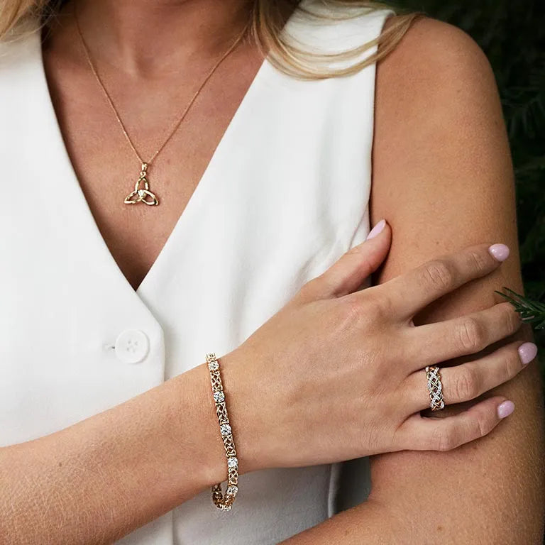 Close-up of a woman wearing gold jewelry including a necklace, bracelet, and ring. 14K Gold| Celtic Eternity Band with Lab Diamonds