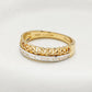 A yellow gold ring with a braided Celtic knot design on the top half and a channel-set row of clear stones on the bottom half, shown on a light textured background. The inside of the band is stamped with '14K GOLD' and 'Shand'.