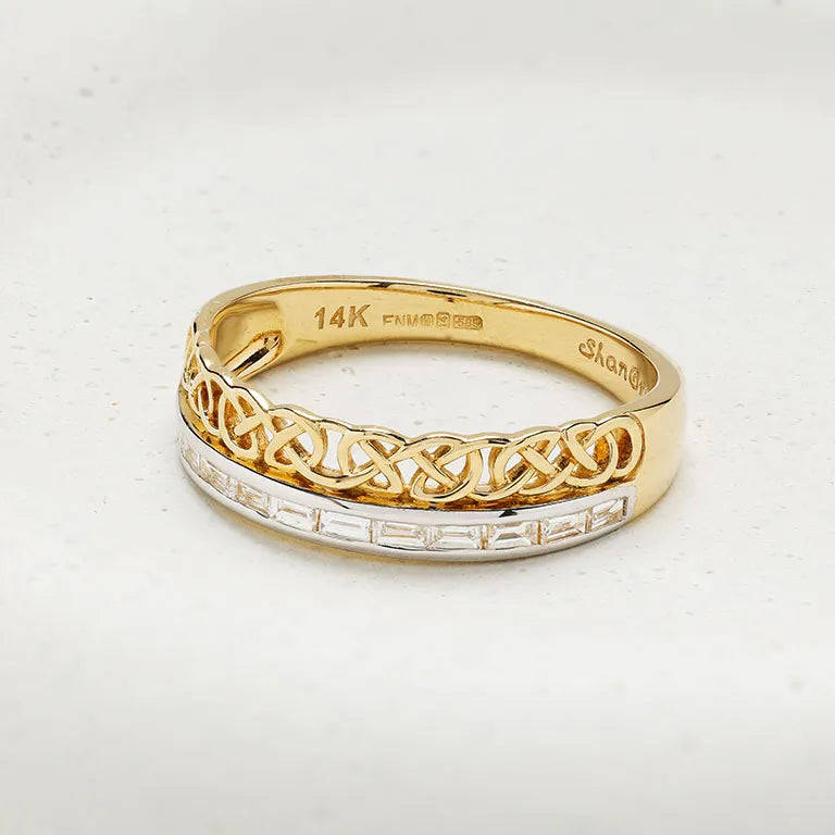 A yellow gold ring with a braided Celtic knot design on the top half and a channel-set row of clear stones on the bottom half, shown on a light textured background. The inside of the band is stamped with '14K GOLD' and 'Shand'.