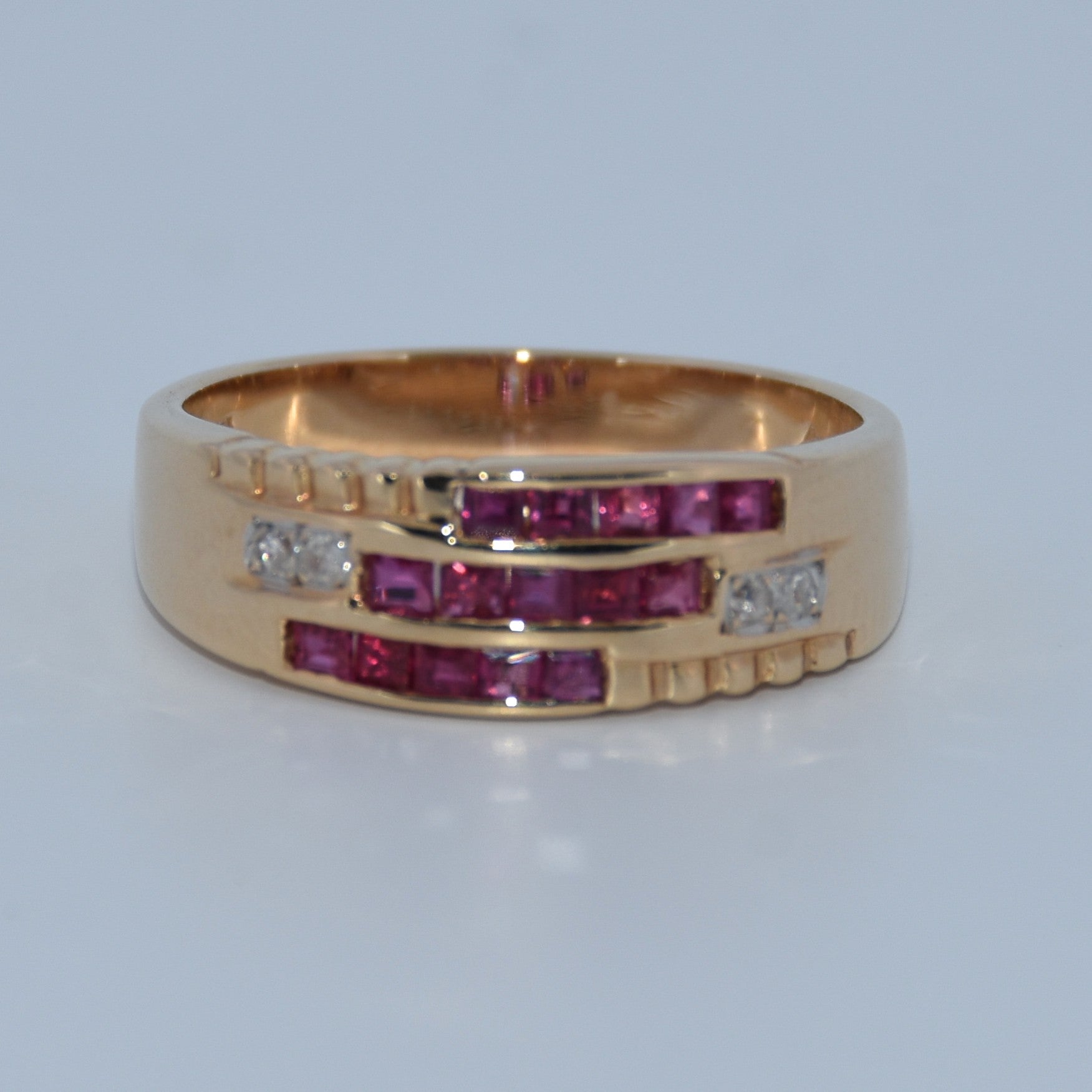 Gold ring with red gemstones and small diamonds on a light gray background