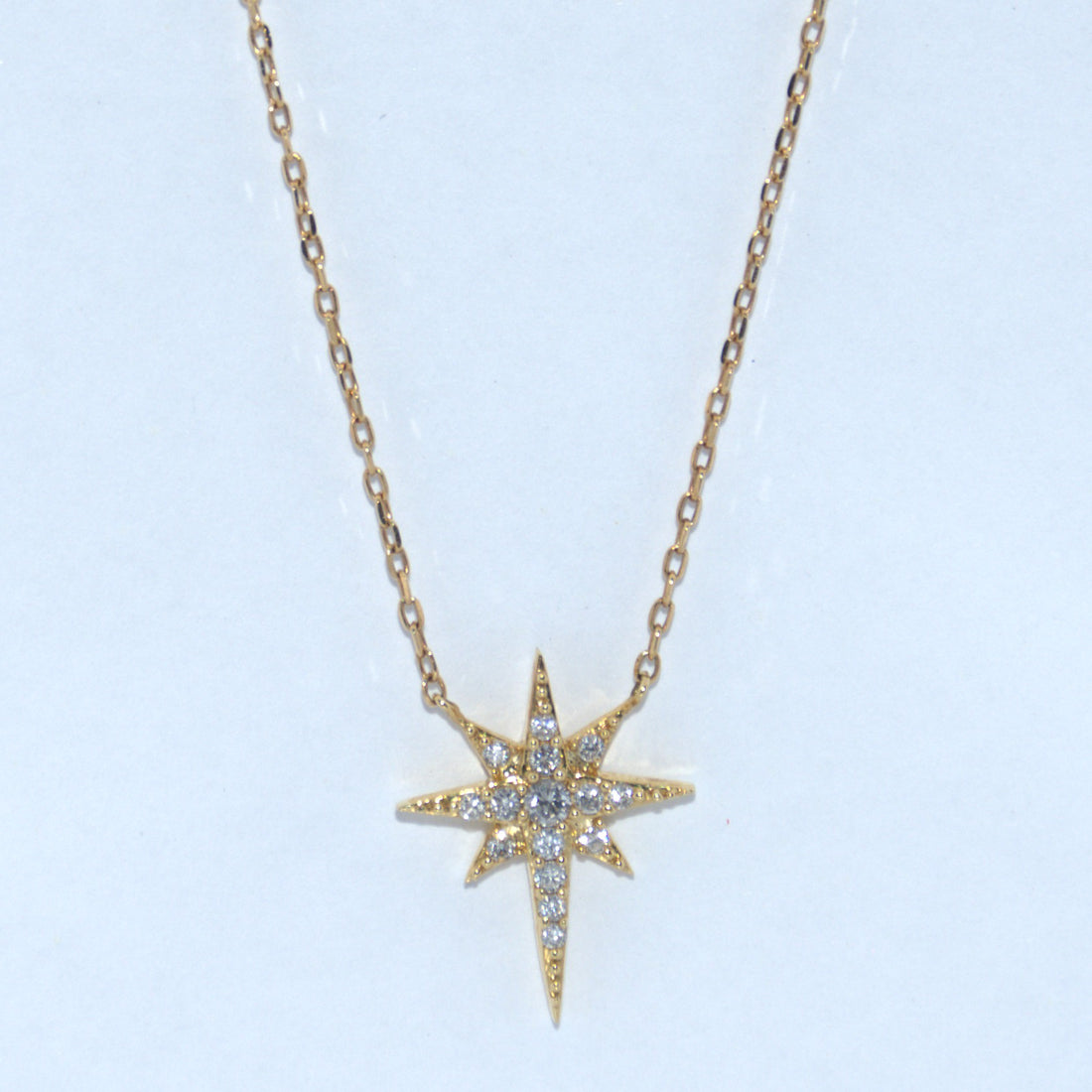 Gold star-shaped necklace with diamonds on a light blue background