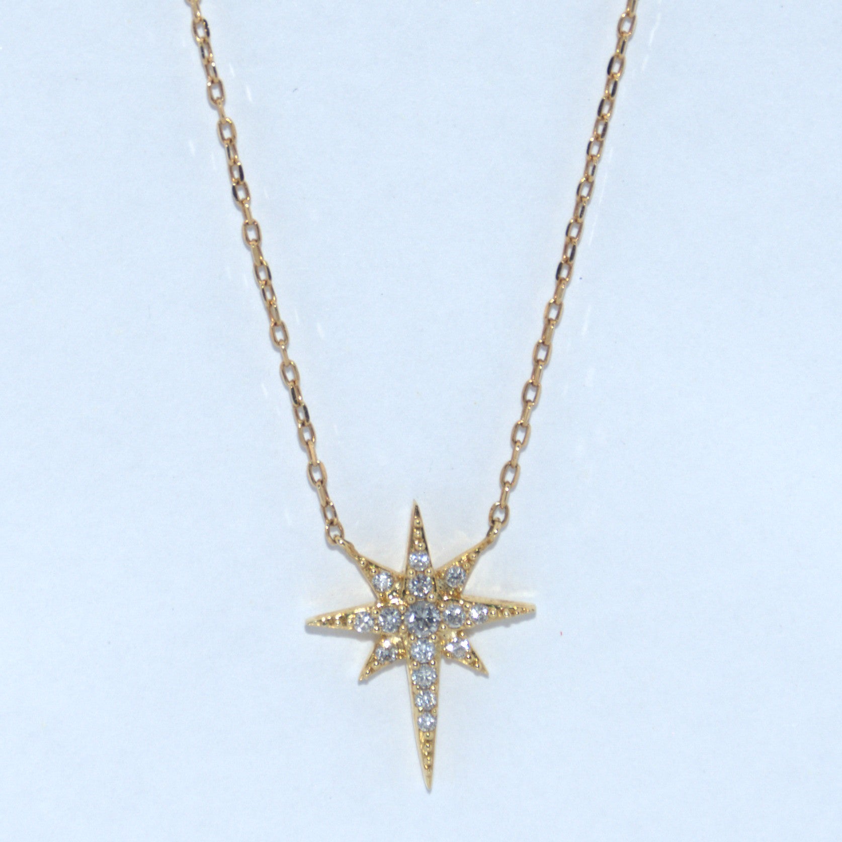 Gold star-shaped necklace with diamonds on a light blue background