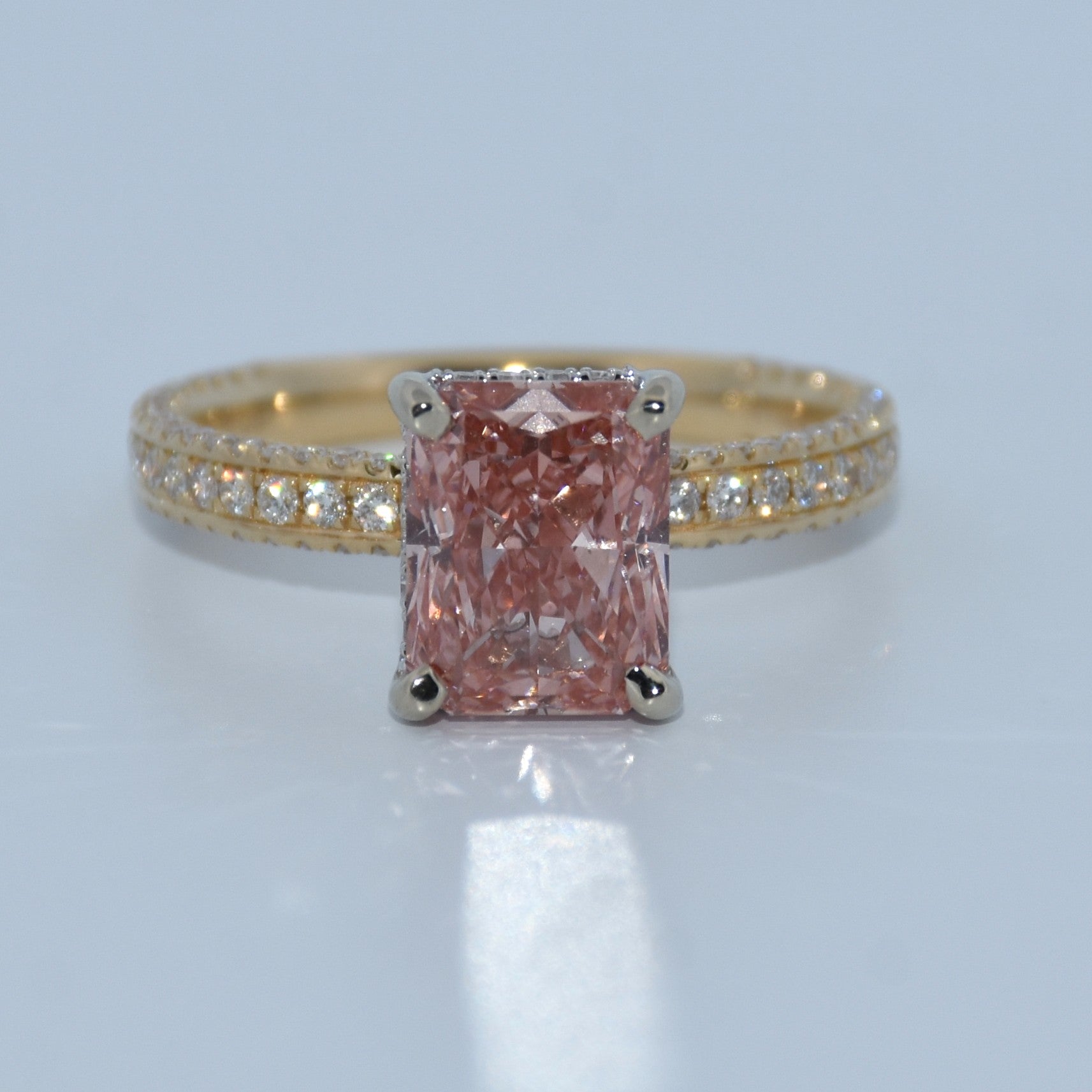 Gold ring with a pink diamond and smaller diamonds on a light gray background