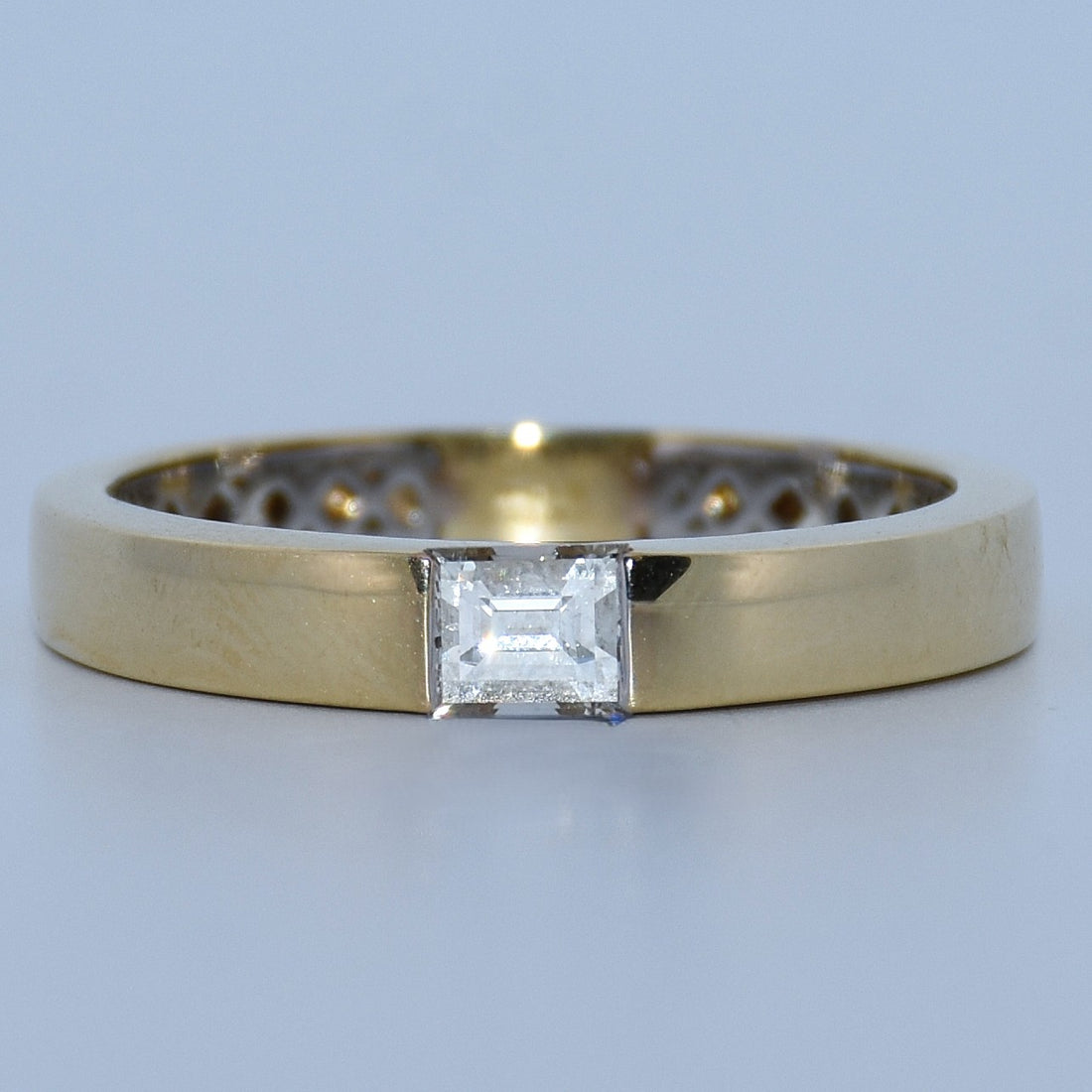Gold ring with a square-cut diamond on a light gray background