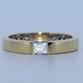 Gold ring with a square-cut diamond on a light gray background