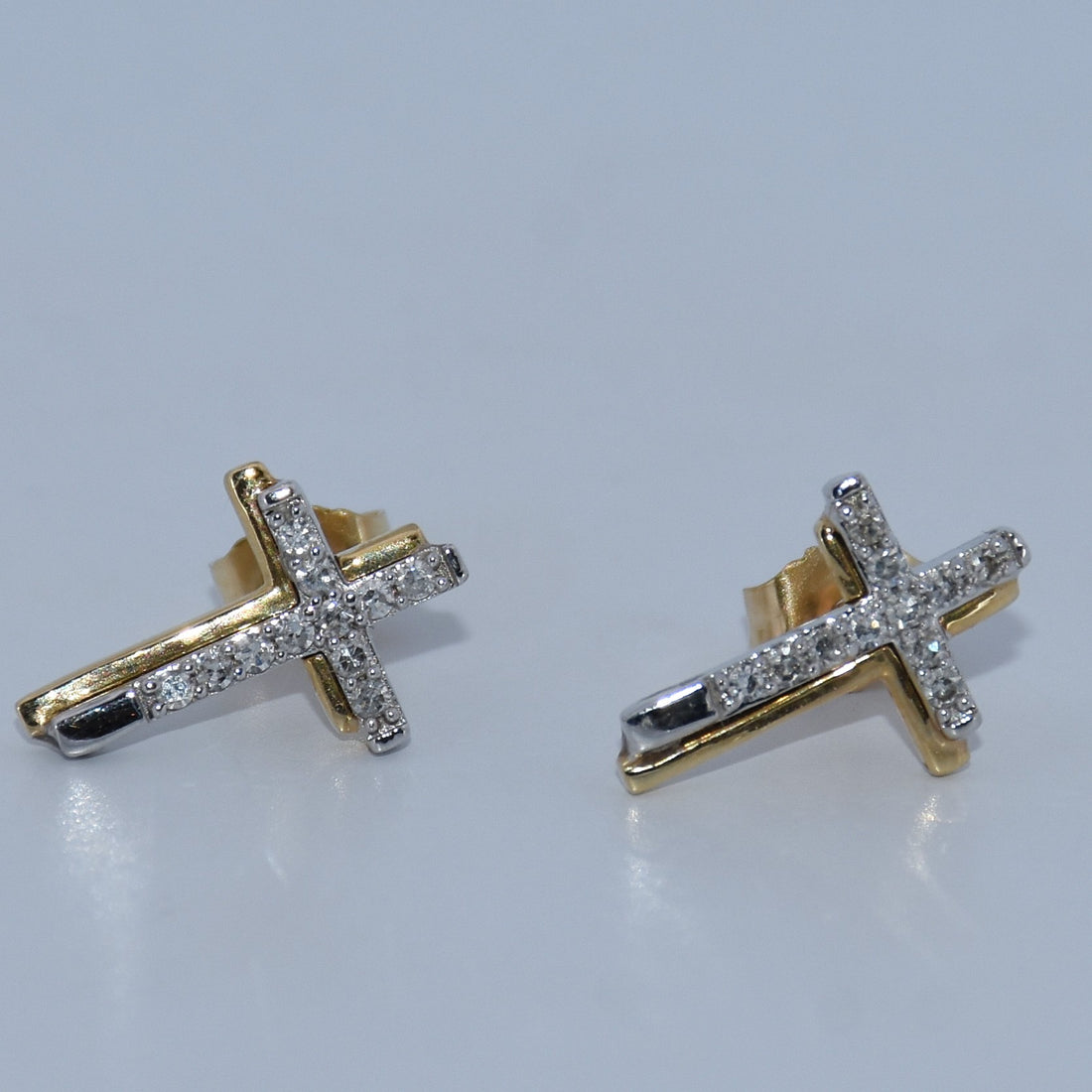 Gold cross earrings with clear stones on a light gray background