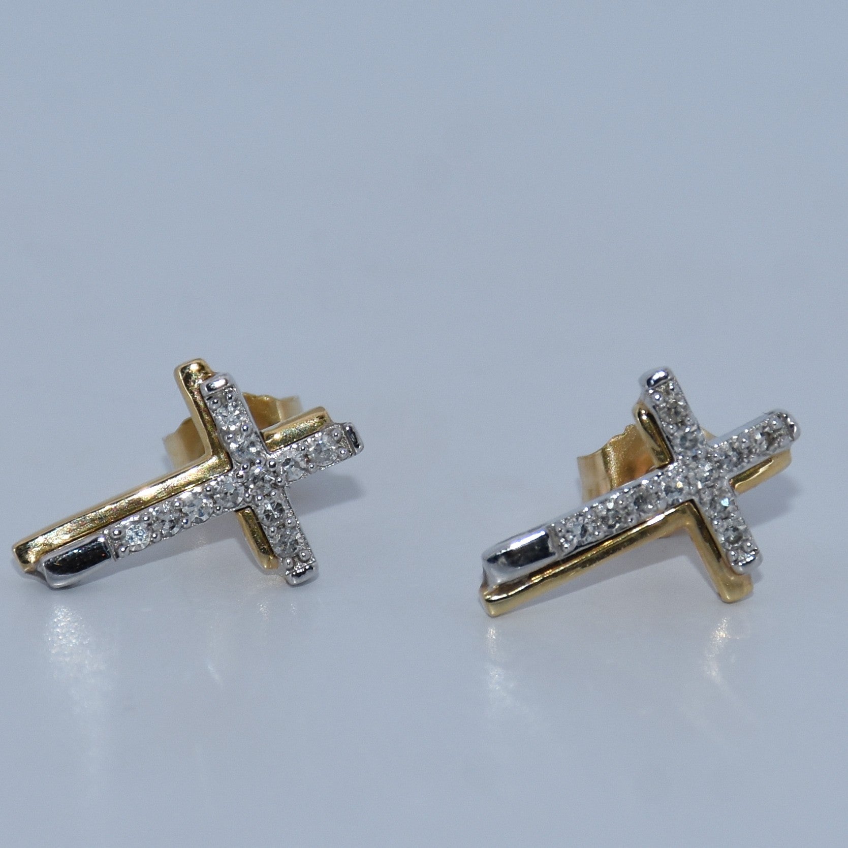 Gold cross earrings with clear stones on a light gray background