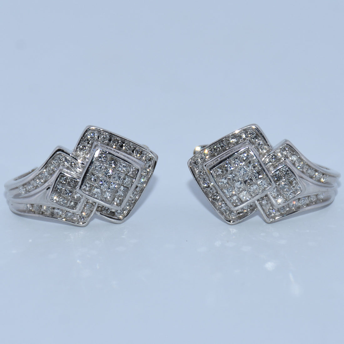 Pair of silver square-shaped earrings with clear stones on a light blue background