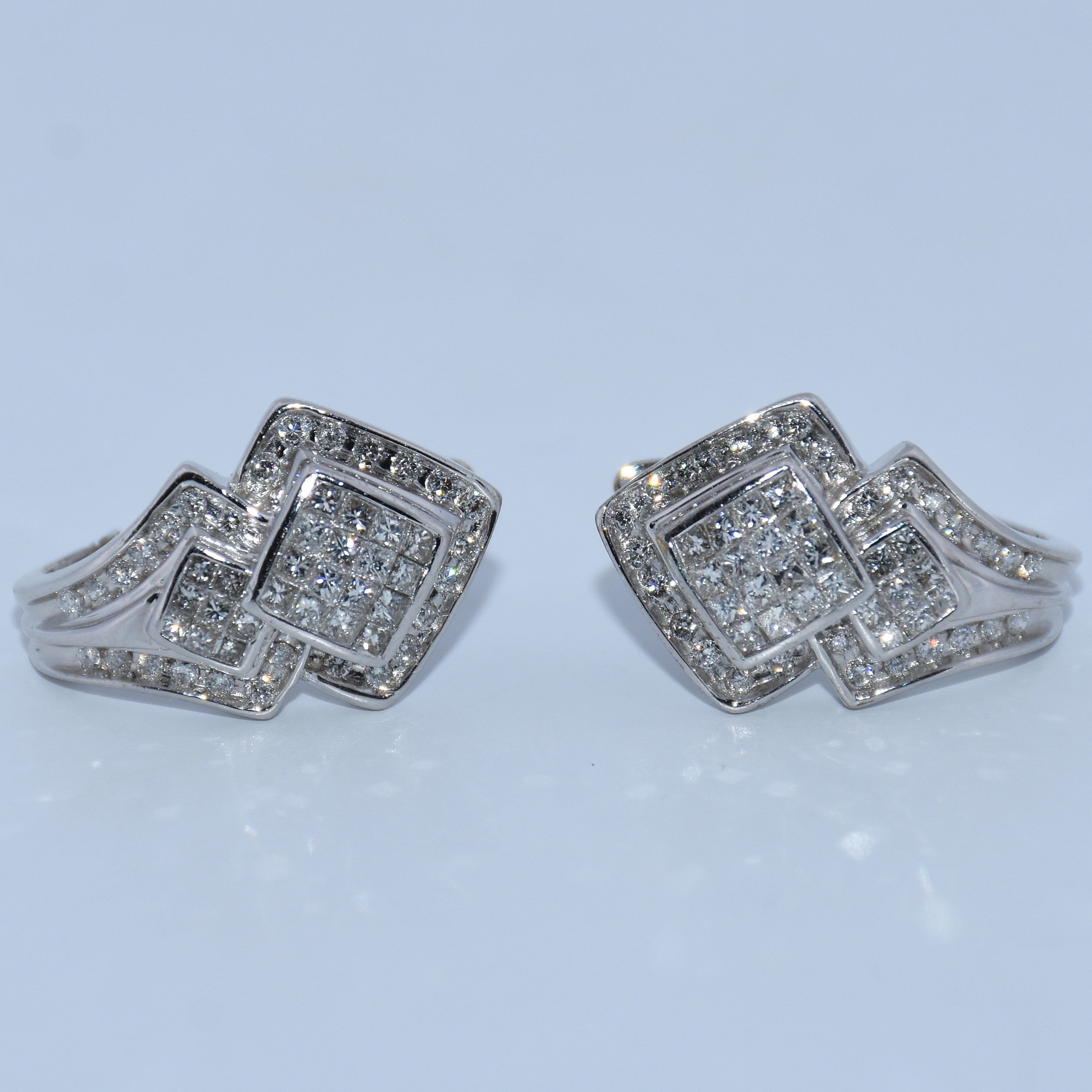 Pair of silver square-shaped earrings with clear stones on a light blue background