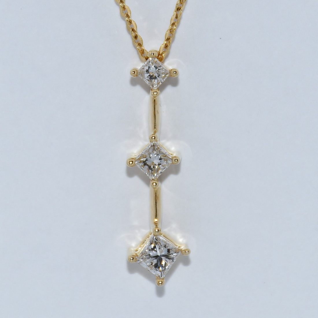 Gold necklace with three diamond pendants on a light gray background