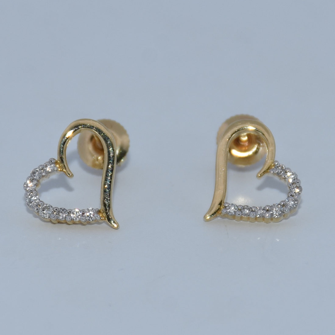 Gold heart-shaped earrings with diamond accents on a light gray background
