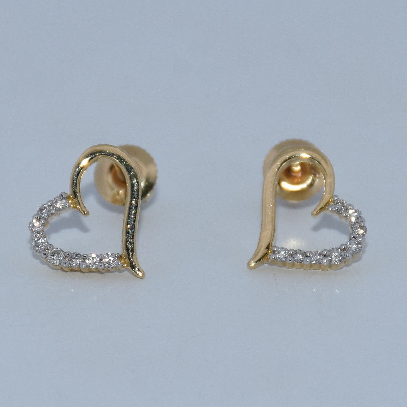 Gold heart-shaped earrings with diamond accents on a light gray background