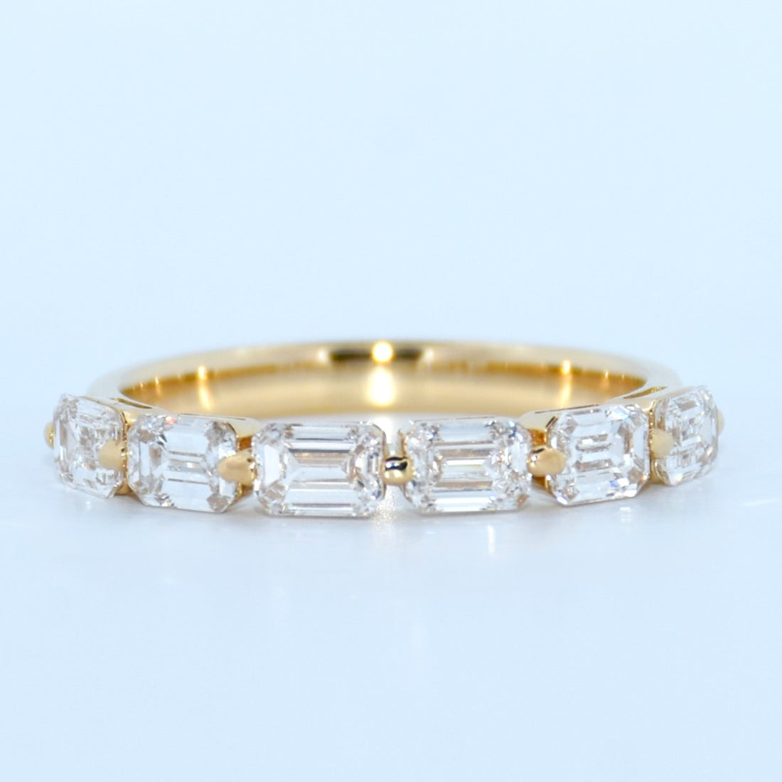 Gold ring with emerald-cut diamonds on a light blue background
