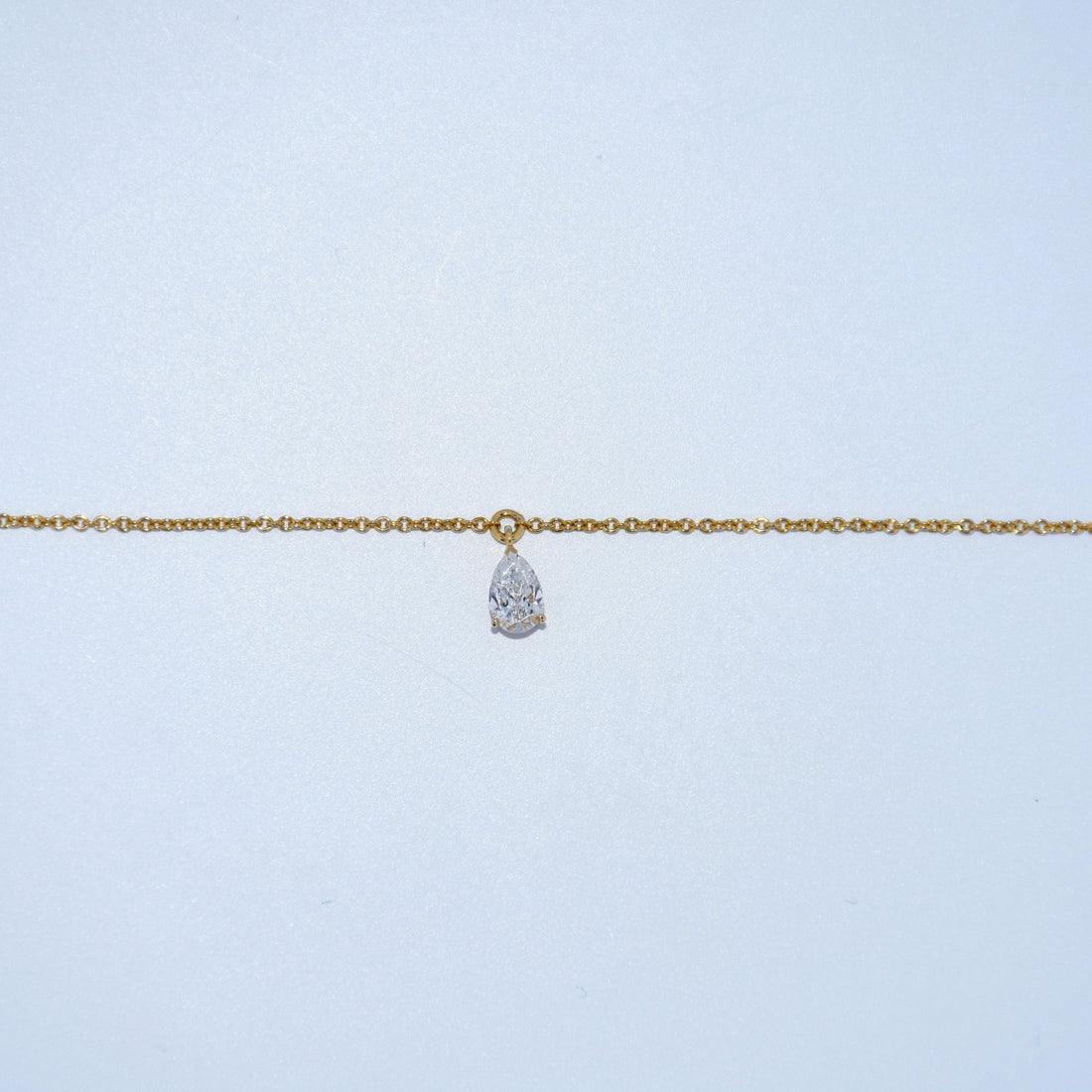 Gold chain necklace with a teardrop-shaped pendant on a light blue background