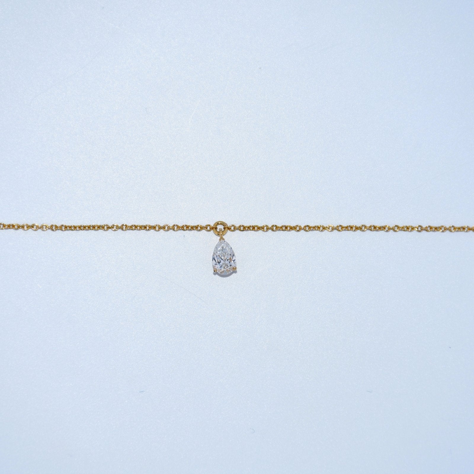 Gold chain necklace with a teardrop-shaped pendant on a light blue background