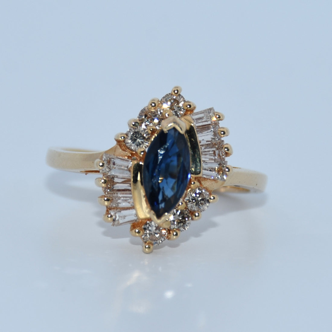 Gold ring with a blue gemstone and diamond accents on a light blue background