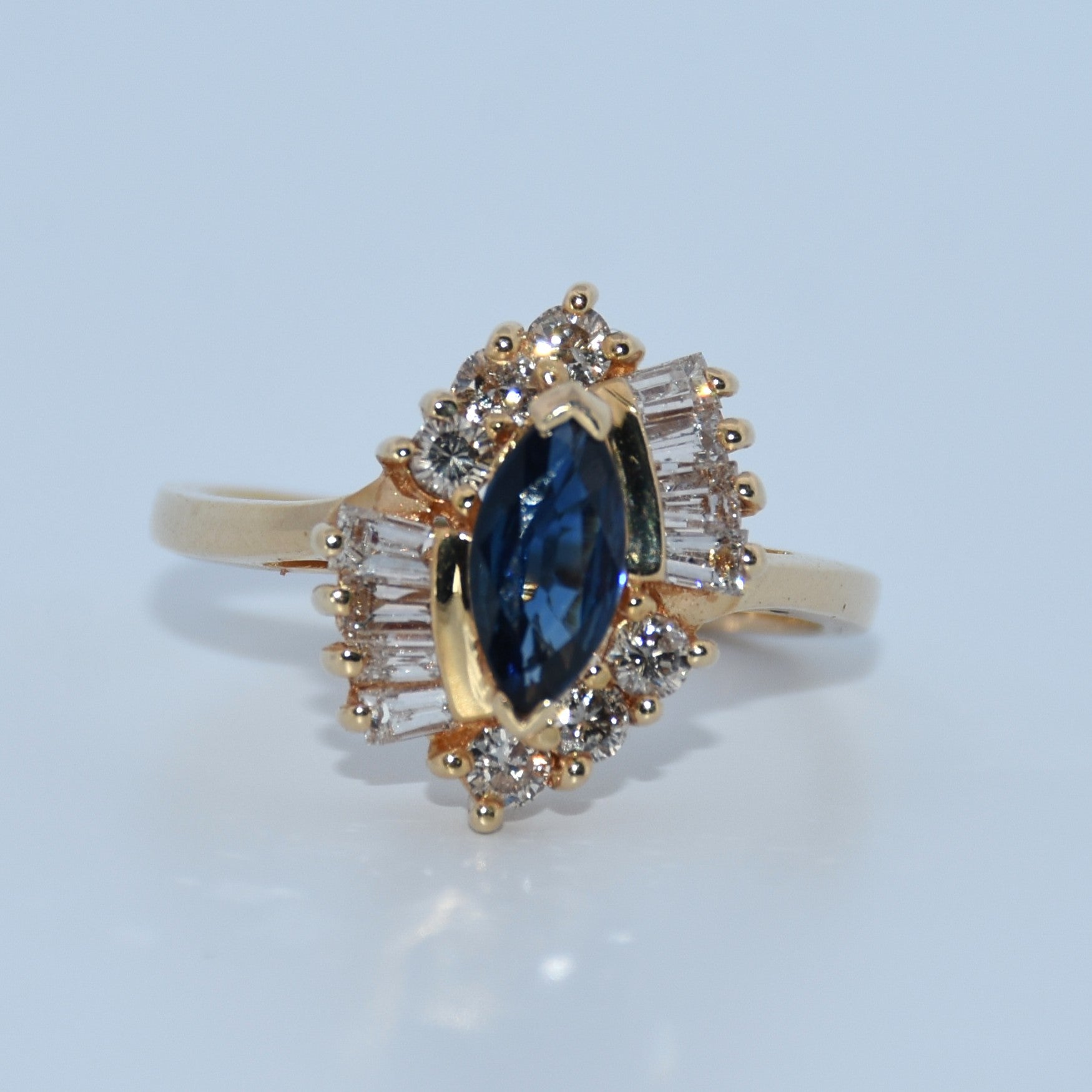 Gold ring with a blue gemstone and diamond accents on a light blue background