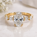 Gold ring with a large diamond and smaller diamonds on the sides, on a soft white background.