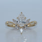 Gold ring with a central pear-shaped diamond and smaller diamonds on a light gray background