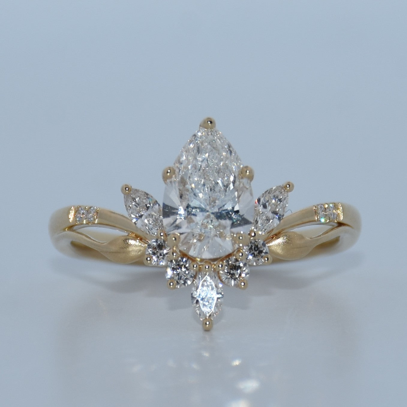 Gold ring with a central pear-shaped diamond and smaller diamonds on a light gray background