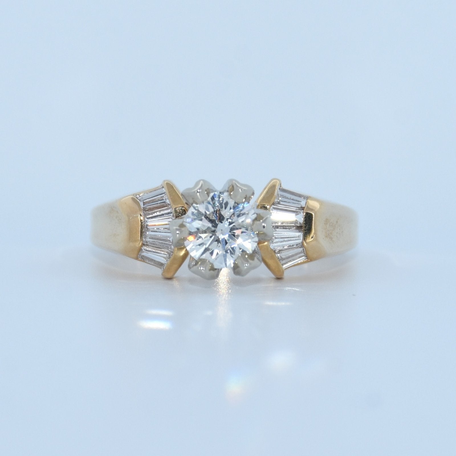 Gold ring with a central diamond and baguette-cut stones on a light blue background