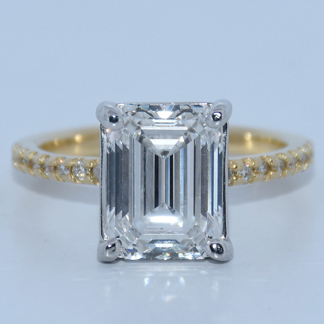 Gold ring with a large emerald-cut diamond and smaller diamonds on a light gray background