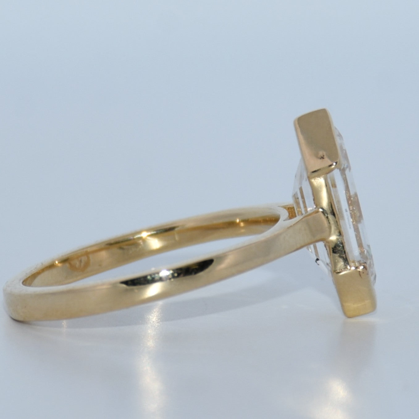 Gold ring with a clear gemstone on a light gray background