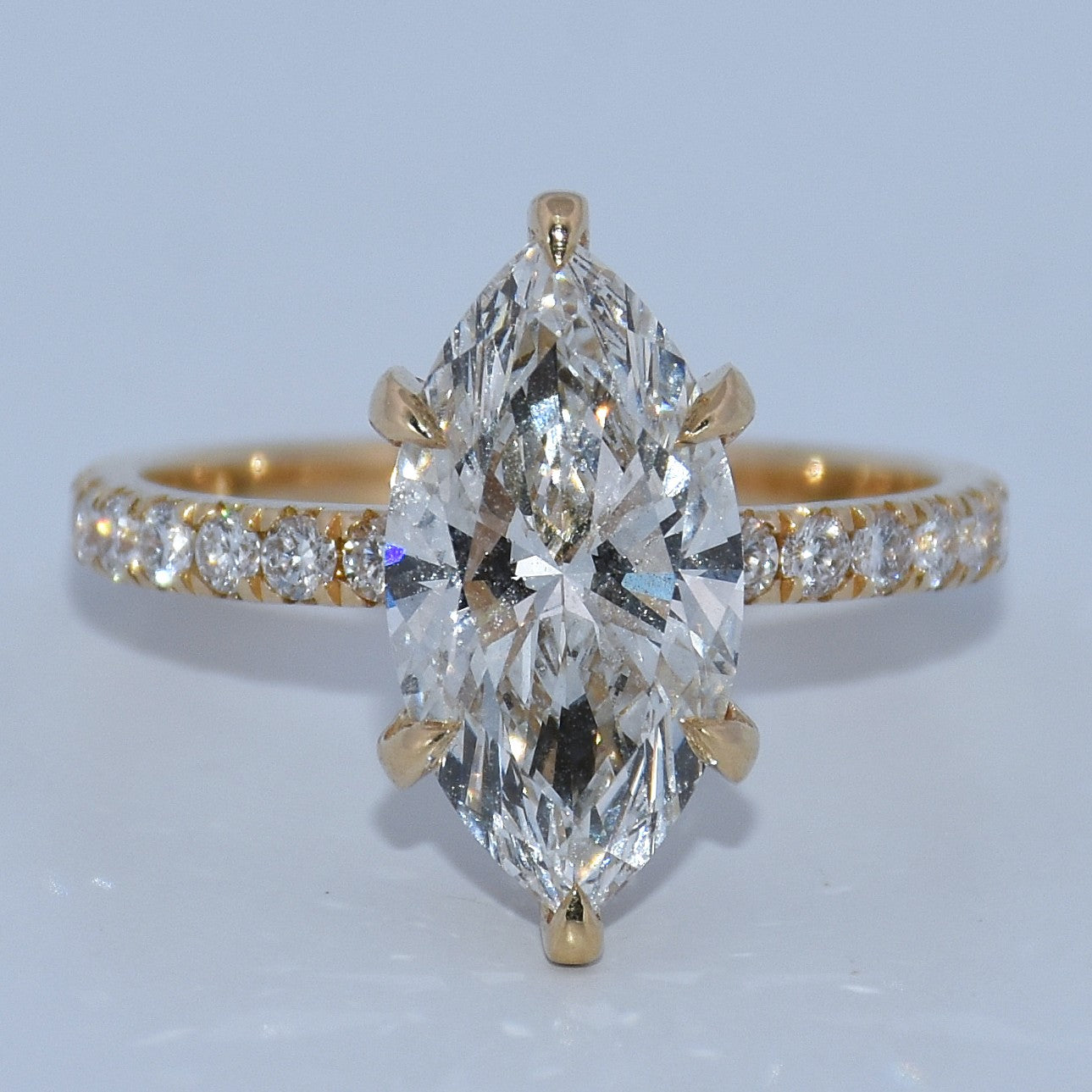 Gold ring with a large marquise-shaped diamond and smaller diamonds on a light gray background