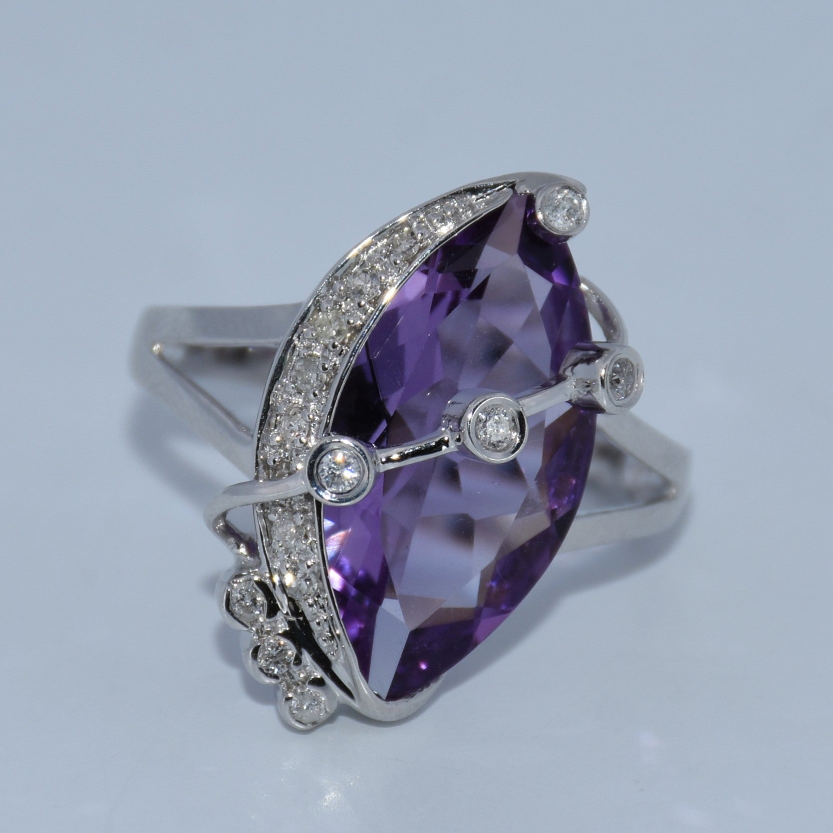 Silver ring with a large purple gemstone on a light gray background