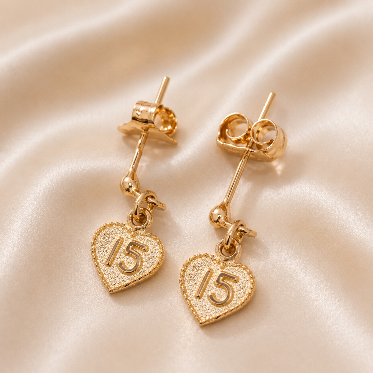 Gold heart-shaped earrings with number '15' on a beige fabric background 19.2K Portuguese Gold | 15th Earrings – Elegant Quinceañera Gold Jewelry