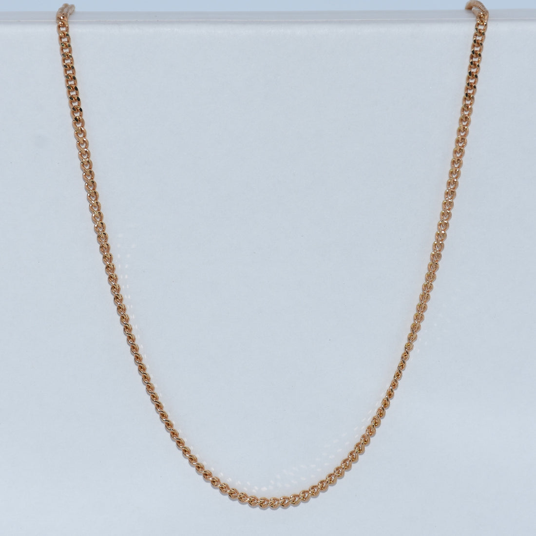 A delicate gold chain necklace draped in a U-shape against a light gray  19.2K Portuguese Gold | 18" 1.5mm Round Solid Curb Chainbackground.
