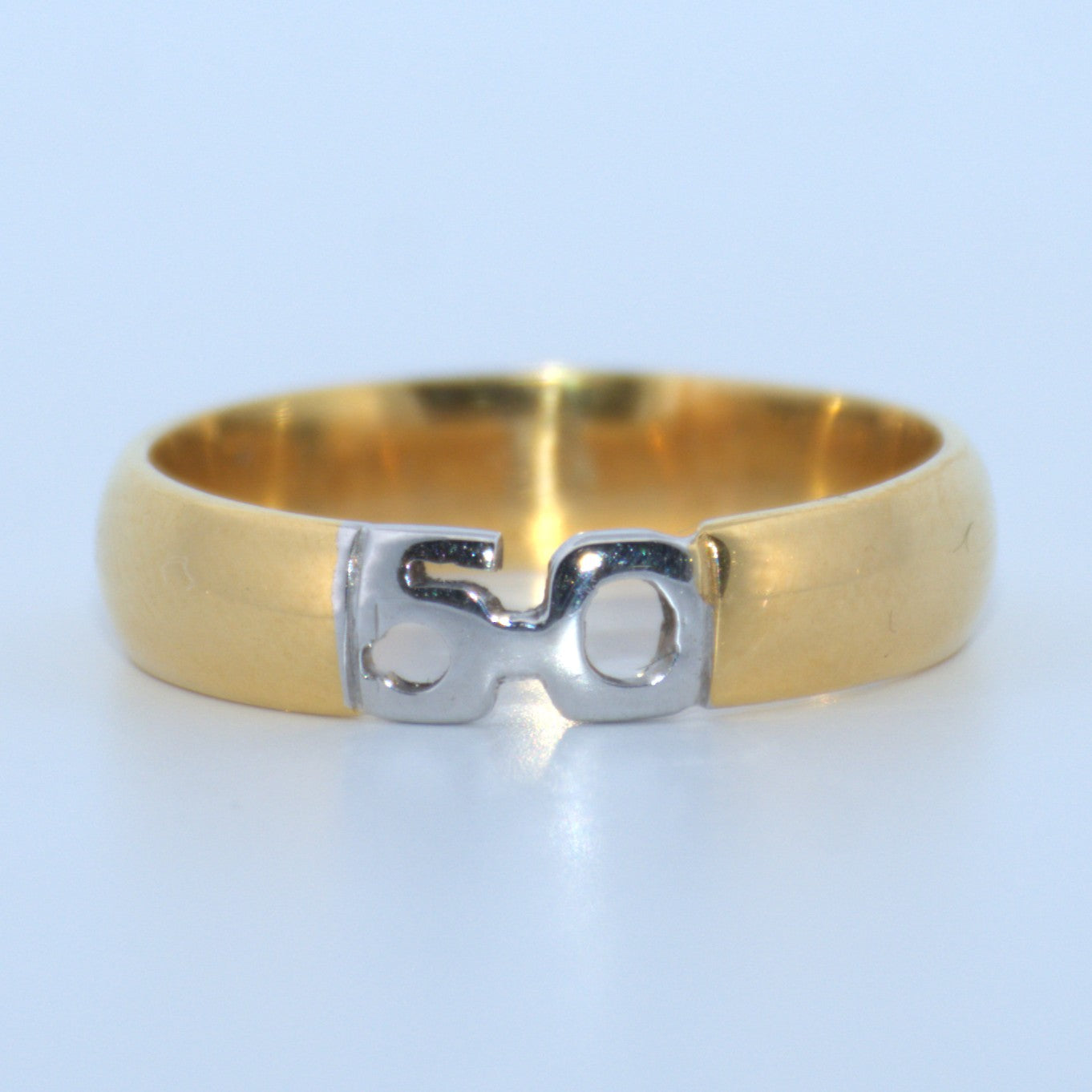 Gold ring with a silver '50' design on a light blue background