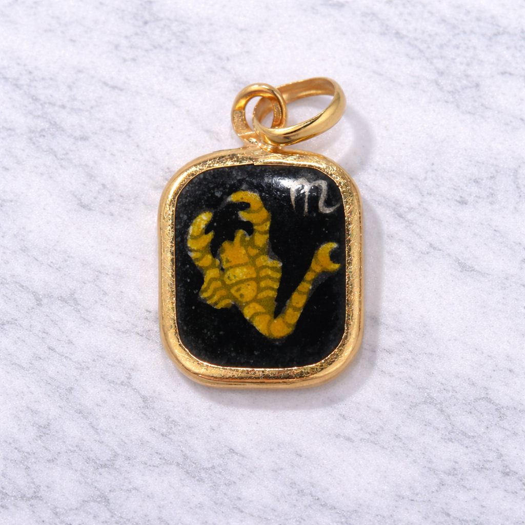 19.2K Portuguese Gold pendant with a black and yellow Scorpio design on a white marble surface